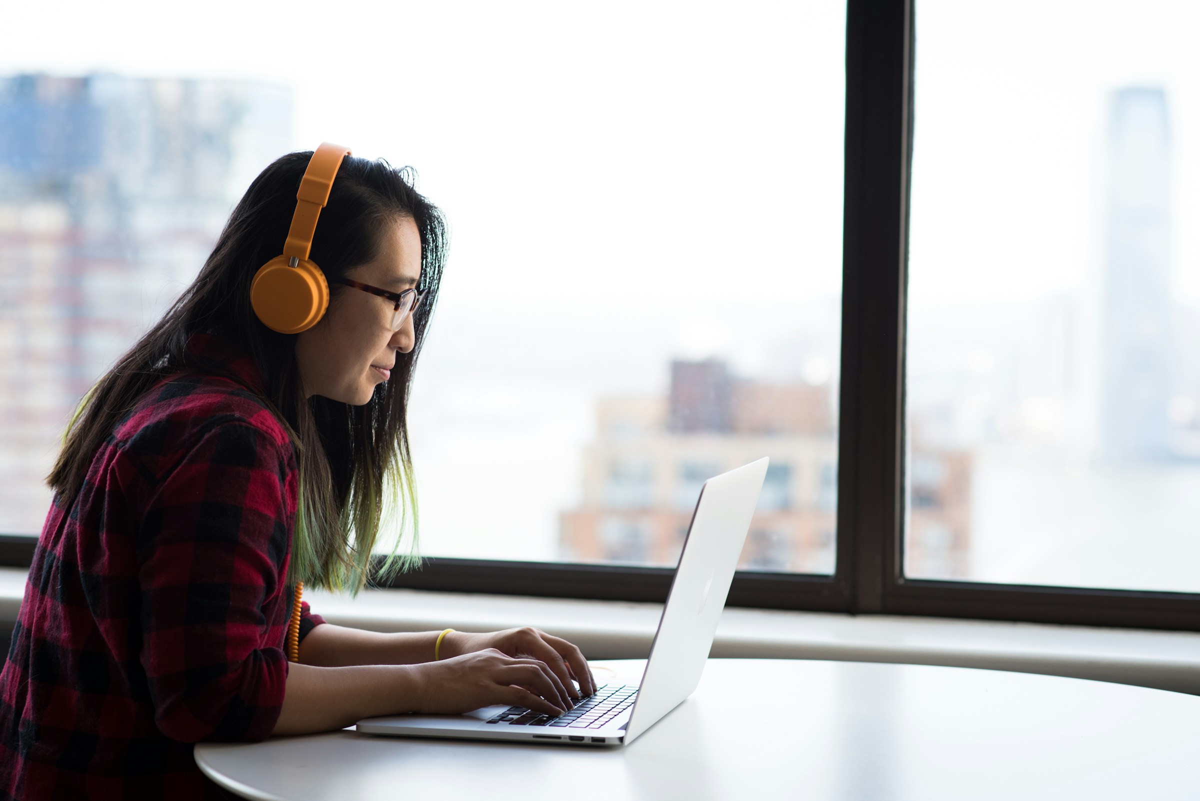 A person in headphones concentrating on work at a MacBook by a window